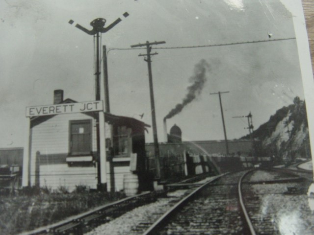 Looking north towards Weyerhauser mill (smokestack). Coast Line to Vancouver to left; mainline at right climbs to upper level of Everett depot then curves east through downtown tunnel.